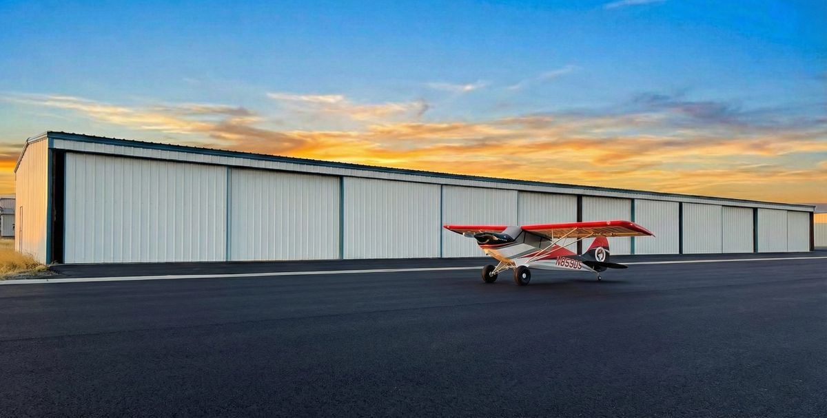 Row of T-hangars at Columbia Gorge Regional Airport at sunset with a red and white taildragger parked in front